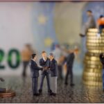 Due lavoratori sorridenti discutono di pensioni anticipate, con grafici e documenti sul tavolo.