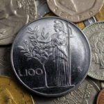 Moneta da 2 Lire con ulivo, esposta su un tavolo con altri oggetti numismatici.